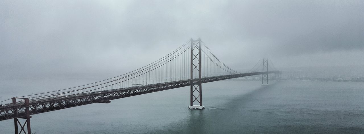 Panoramic view of april 25th bridge over river during foggy weather