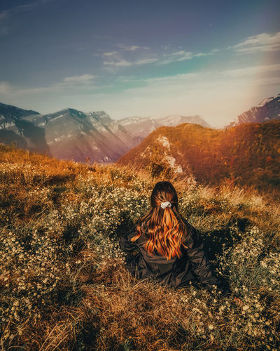 Rear view of woman sitting on landscape against sky