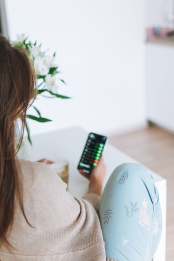 Young woman checking cryptocurrency charts and stock quotes on mobile phone with cup of coffee 