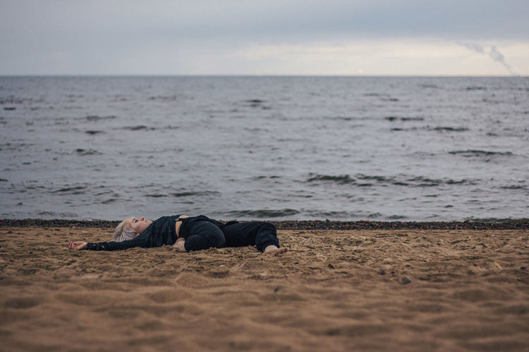 Man lying on shore at beach against sky