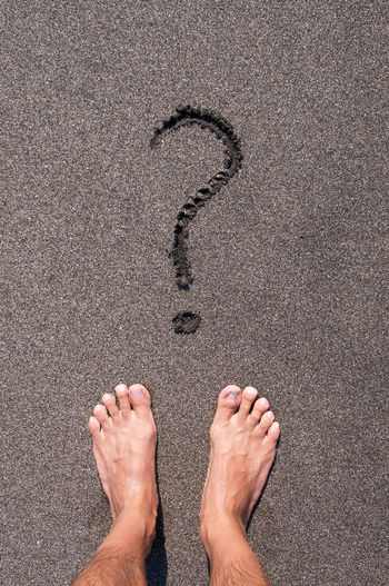 Low section of man standing by question mark on wet sand