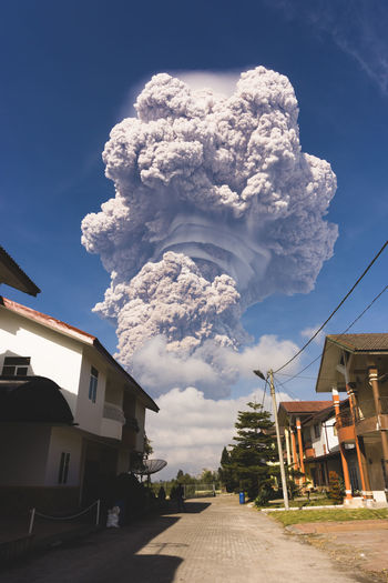 Low angle view of erupting volcano seen from city