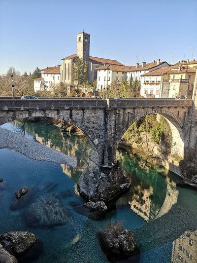 Bridge over river by buildings against sky