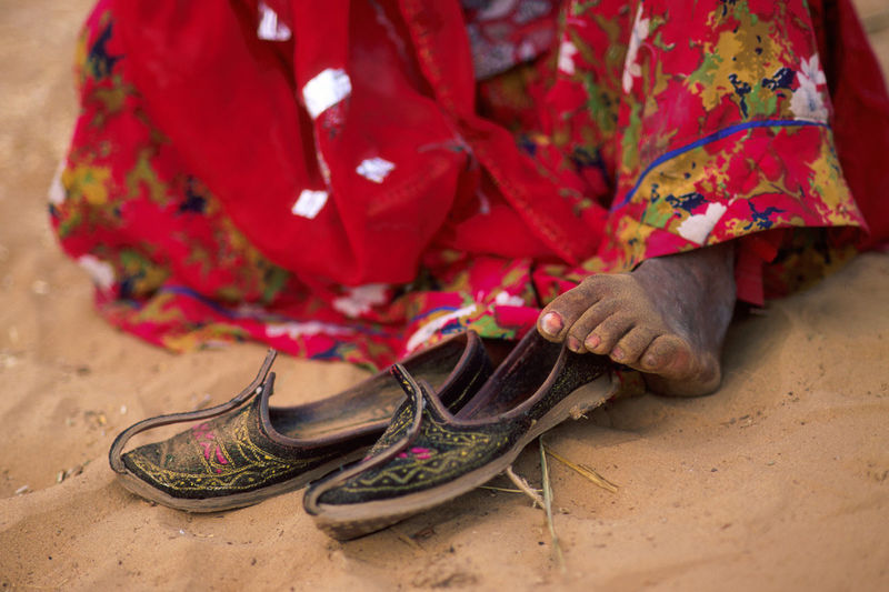 Low section of woman wearing shoes and traditional clothing sitting on sand in desert
