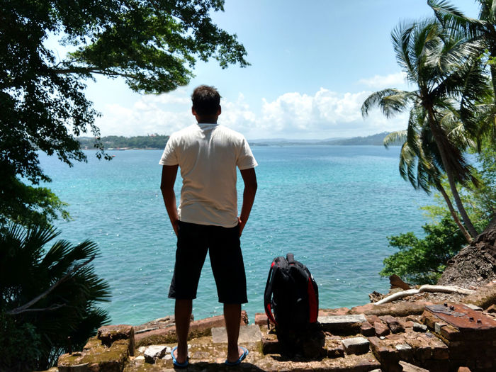 Rear view of traveler with backpack standing by sea against sky