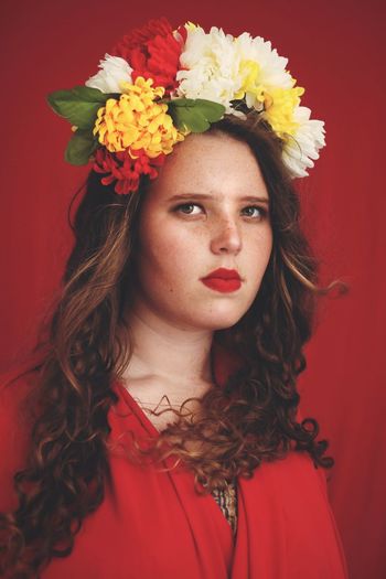 Portrait of young woman wearing floral crown against red background