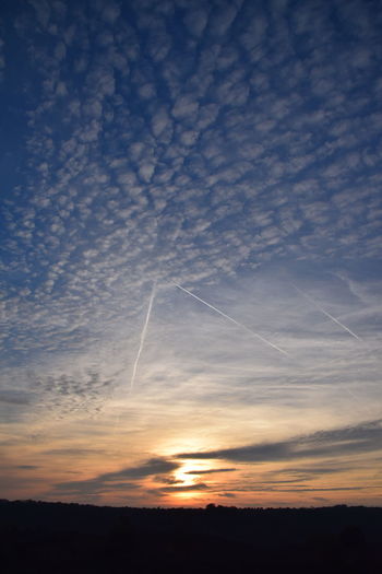 Low angle view of vapor trails in sky during sunset