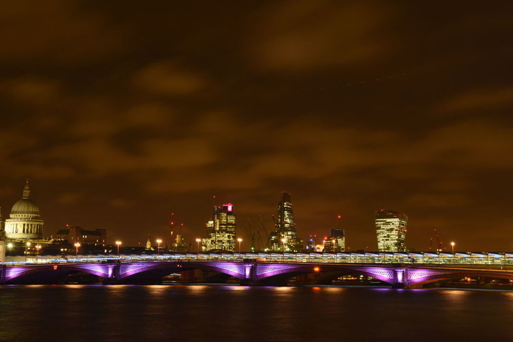 Illuminated cityscape with blackfriars bridge over thames river against cloudy sky