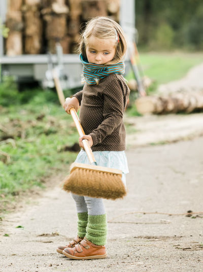 Side view of girl holding broom while standing on road