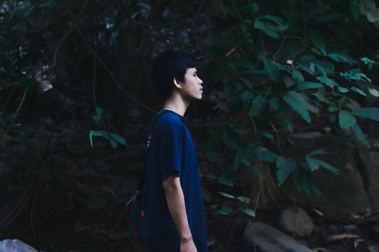 Side view of young man looking away in forest