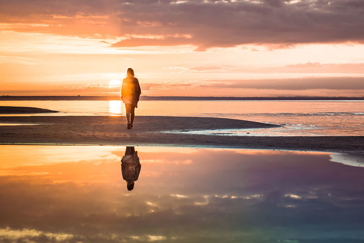 Full length of silhouette woman walking at beach during sunset