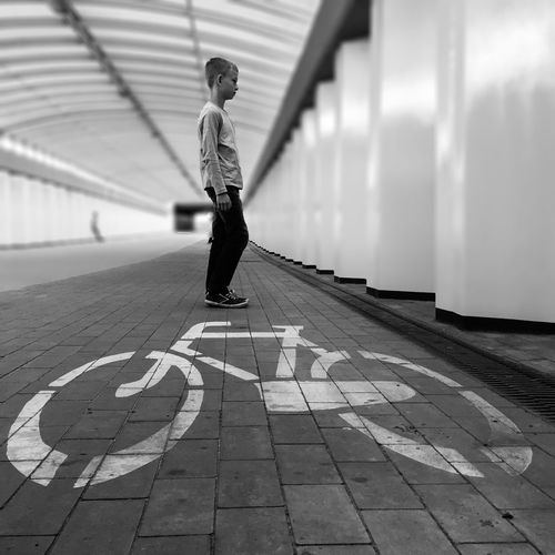 Full length of boy standing by bicycle lane symbol at bridge
