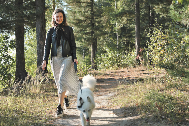 Young woman walking in the forest with a dog. sunny fall day. smiling woman wearing dress. 