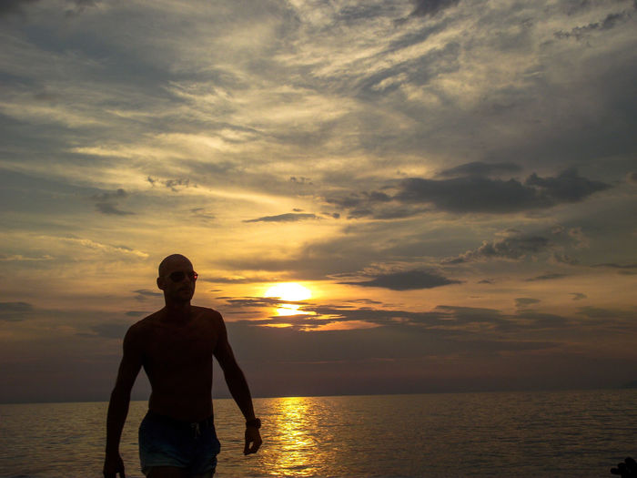 Man at beach against sky during sunset
