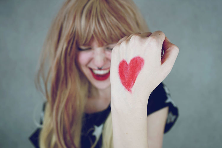 Happy young woman with heart shape on hand against gray background