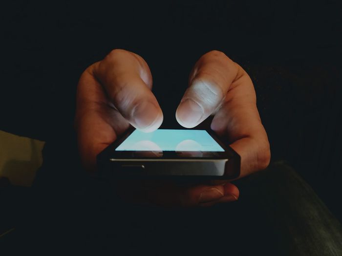 Close-up of hand holding mobile phone against black background