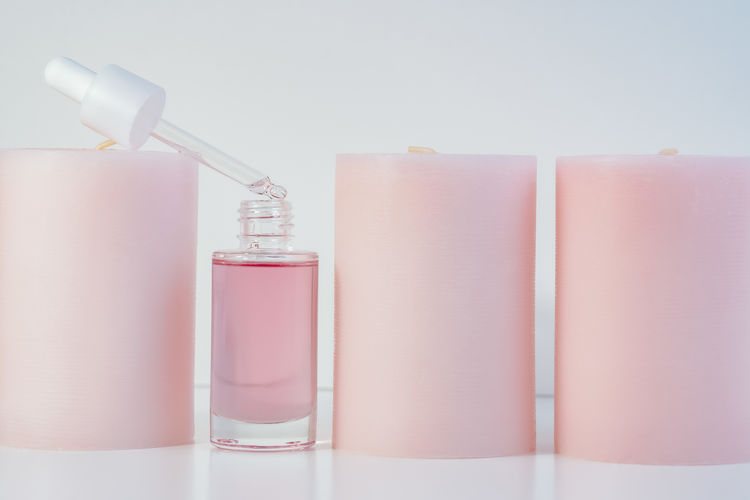 Pink face oil in glass bottle with white cap and big round candles in a row