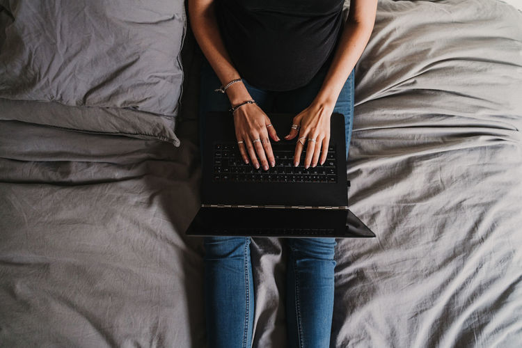 Midsection of pregnant woman using laptop while sitting on bed at home