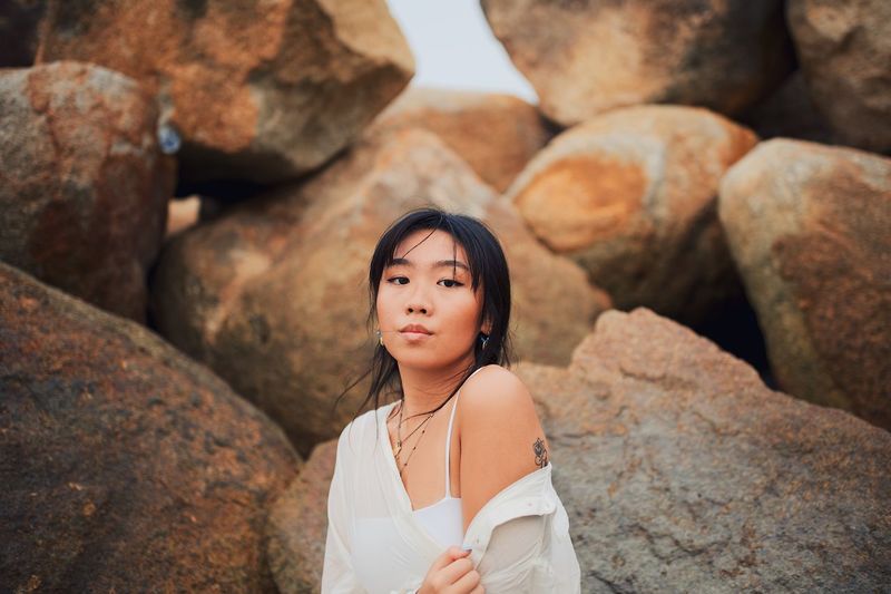 PORTRAIT OF BEAUTIFUL YOUNG WOMAN STANDING ON ROCK