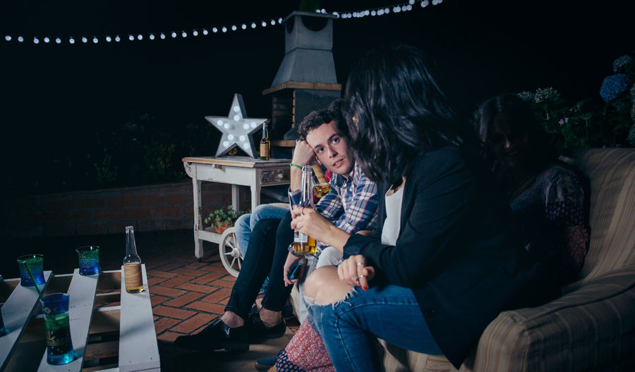 Friends sitting on sofa at patio during night