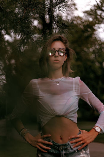 Young woman wearing sunglasses standing against trees