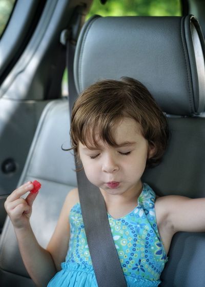Close-up of girl eating candy while sitting with eyes closed in car