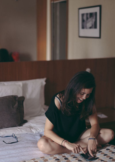 A girl sitting in the bed, reading emails using a smartphone with glasses off