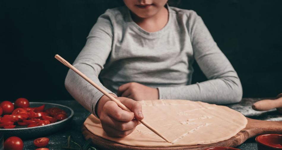 A child's hand draws a christmas tree with a wooden stick on pizza dough