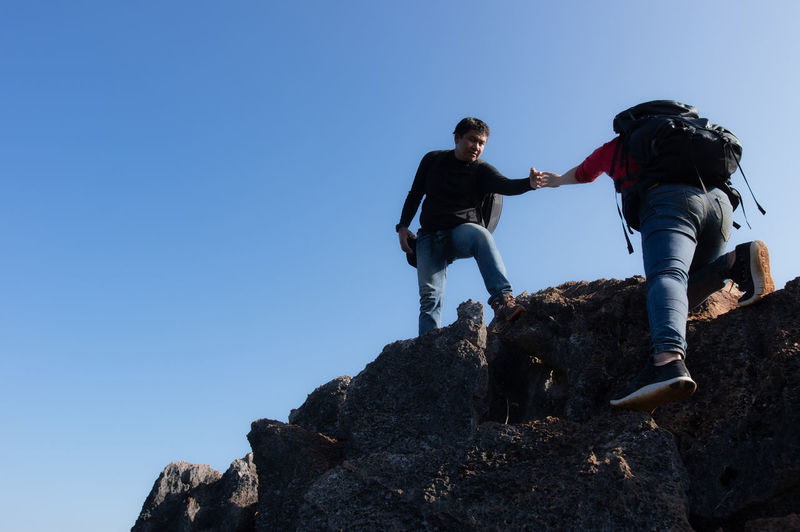 Low angle view of men on rock against clear blue sky