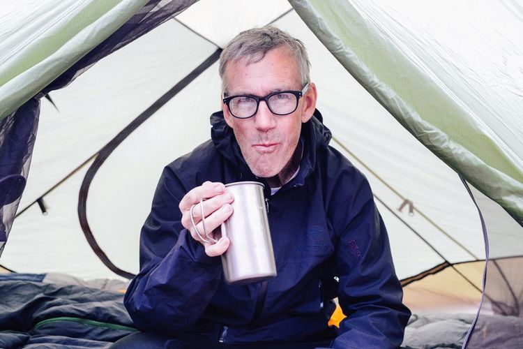 Man in camping tent drinking from tin mug