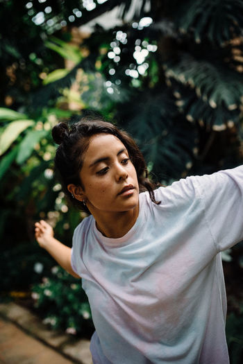 Latina girl with boho shirt dancing surrounded by green leaves