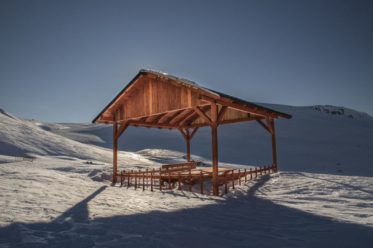 Gazebo on snow covered land against clear sky