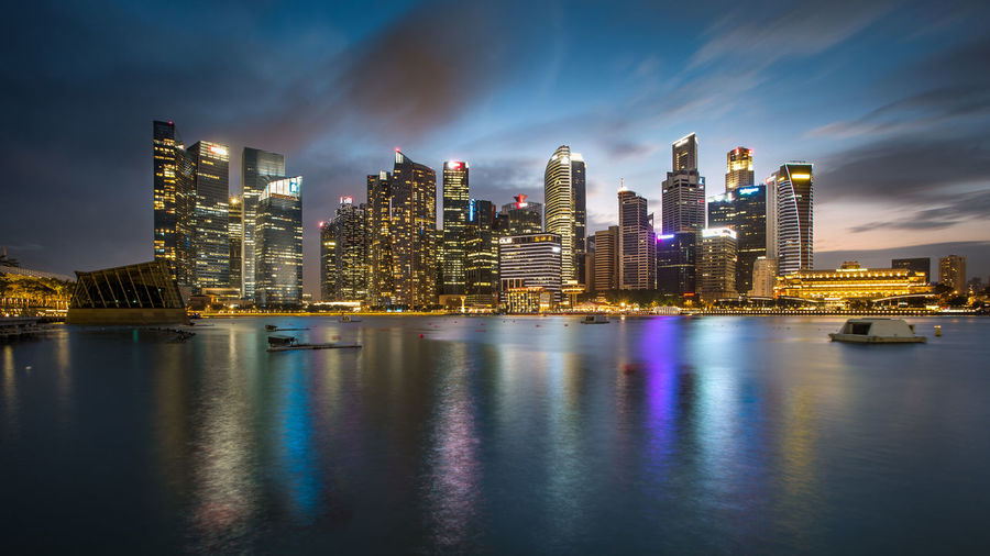 Illuminated buildings by river against sky in city