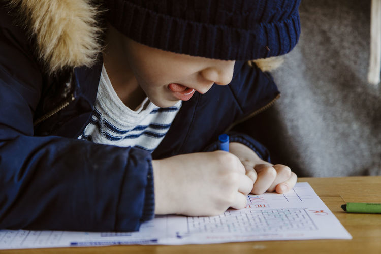 Boy coloring at restaurant table while waiting sticking tongue out