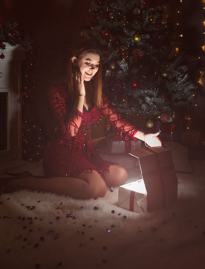 Young woman sitting on christmas tree at home