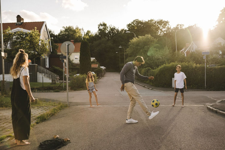 Father playing with soccer ball with family on road