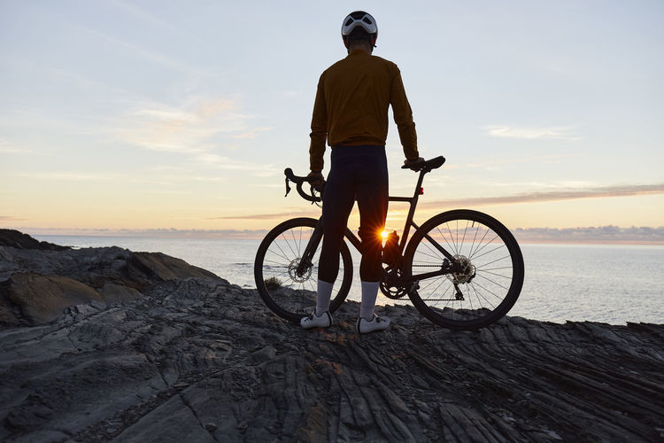 Cyclist standing with bicycle in front of sea at sunrise