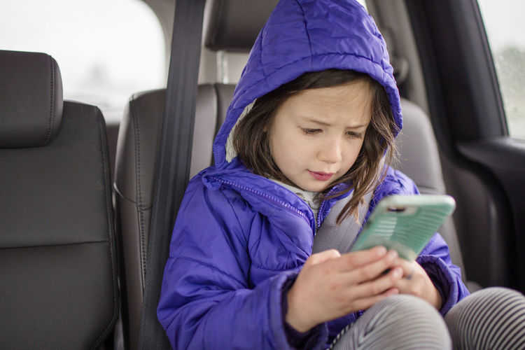 A little girl plays with phone in the backseat of a car on a car trip