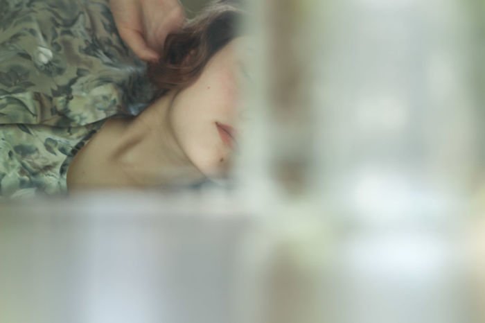 Midsection of young woman relaxing on bed seen through window
