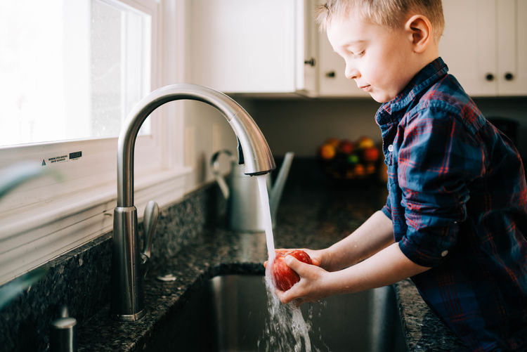 Side view of boy with faucet in water at home