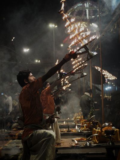 Side view of people rotating flame while praying at riverbank during night