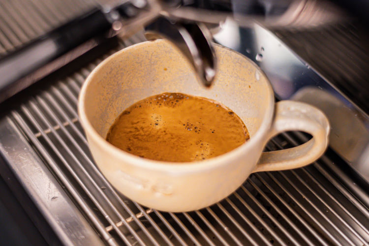 Preparing coffee with bar coffee machine, coffee is poured in a ceramic cup, close up