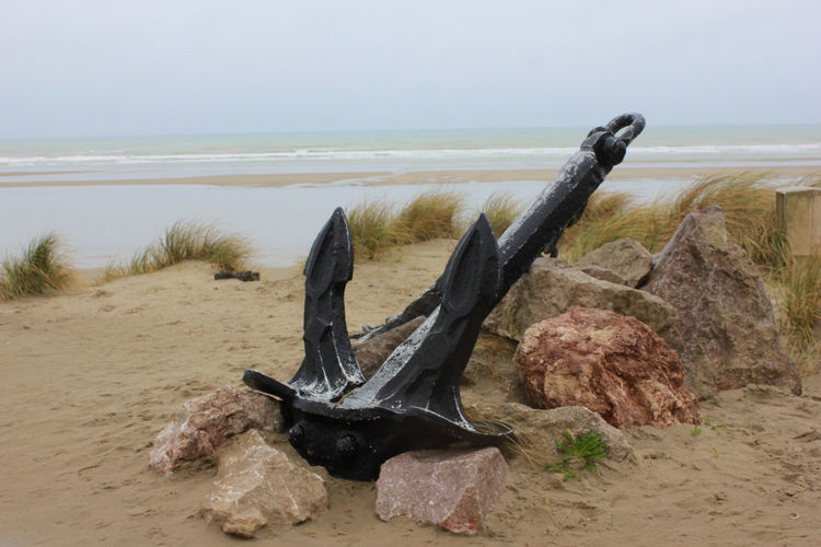 Abandoned black anchor at sandy beach against clear sky