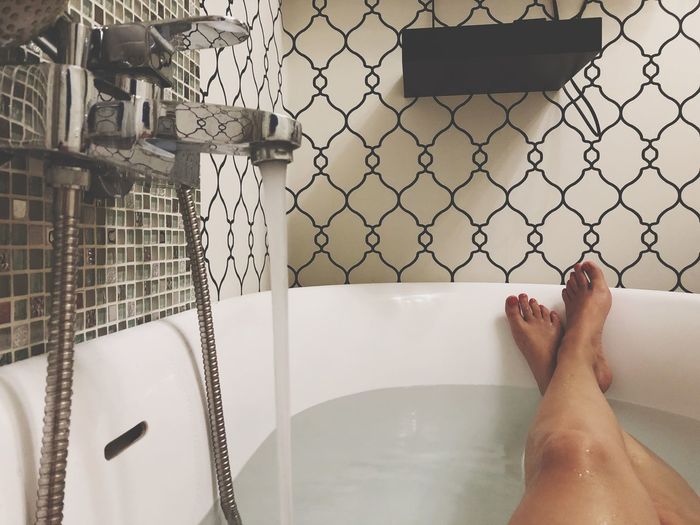 Low section of woman relaxing in bathtub at bathroom
