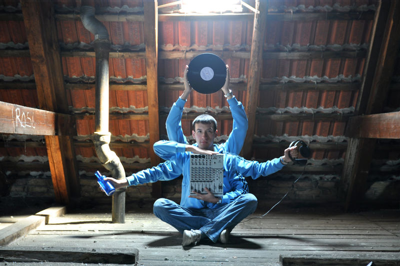Portrait of man holding musical equipment sitting on floor at home