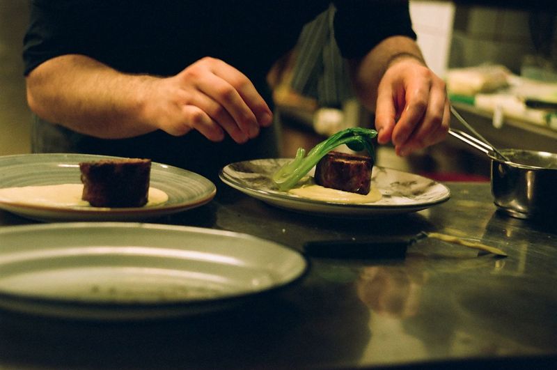 Cropped hands of chef preparing food in plate at kitchen
