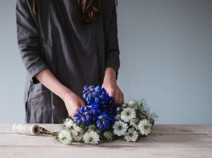 Midsection of woman tying flowers at table against wall