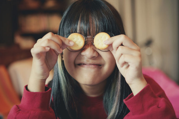 Close-up of smiling girl holding snack against face