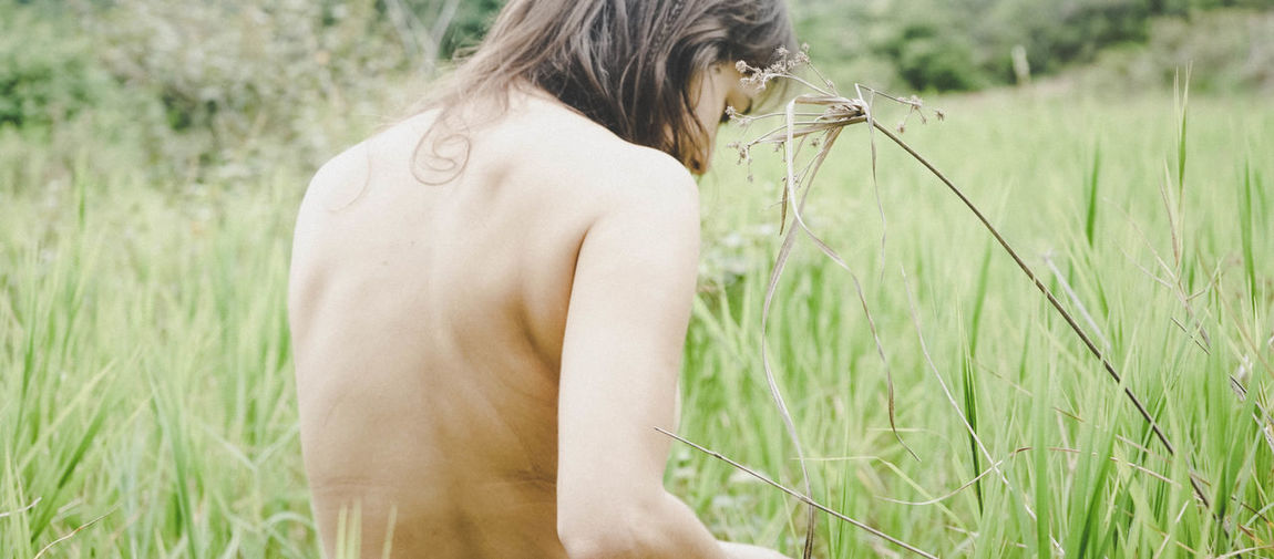 Rear view of shirtless woman sitting on field