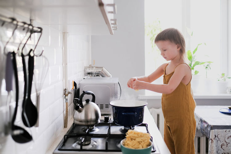 Cute toddler child in kitchen by stove helps mom cook, bright interior of kitchen